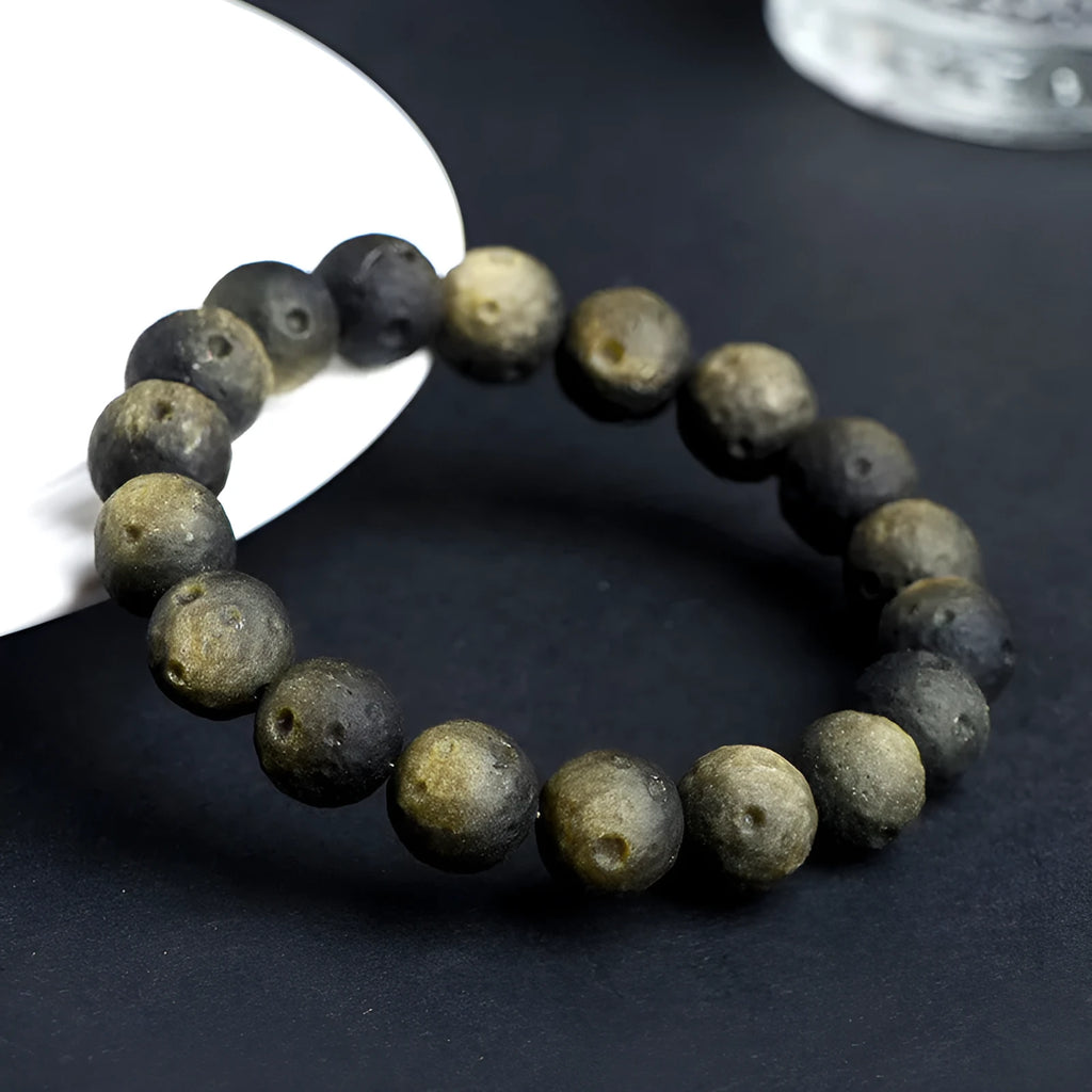Natural obsidian crater ball bracelet with textured beads in silver stone meteorite colour on a wrist.