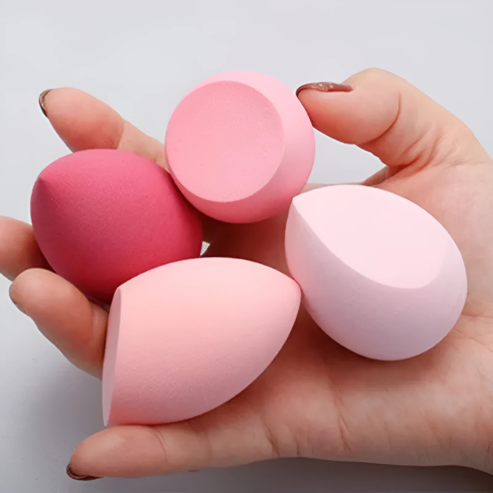 Set of seven differently shaped makeup sponges in various colours on pink background