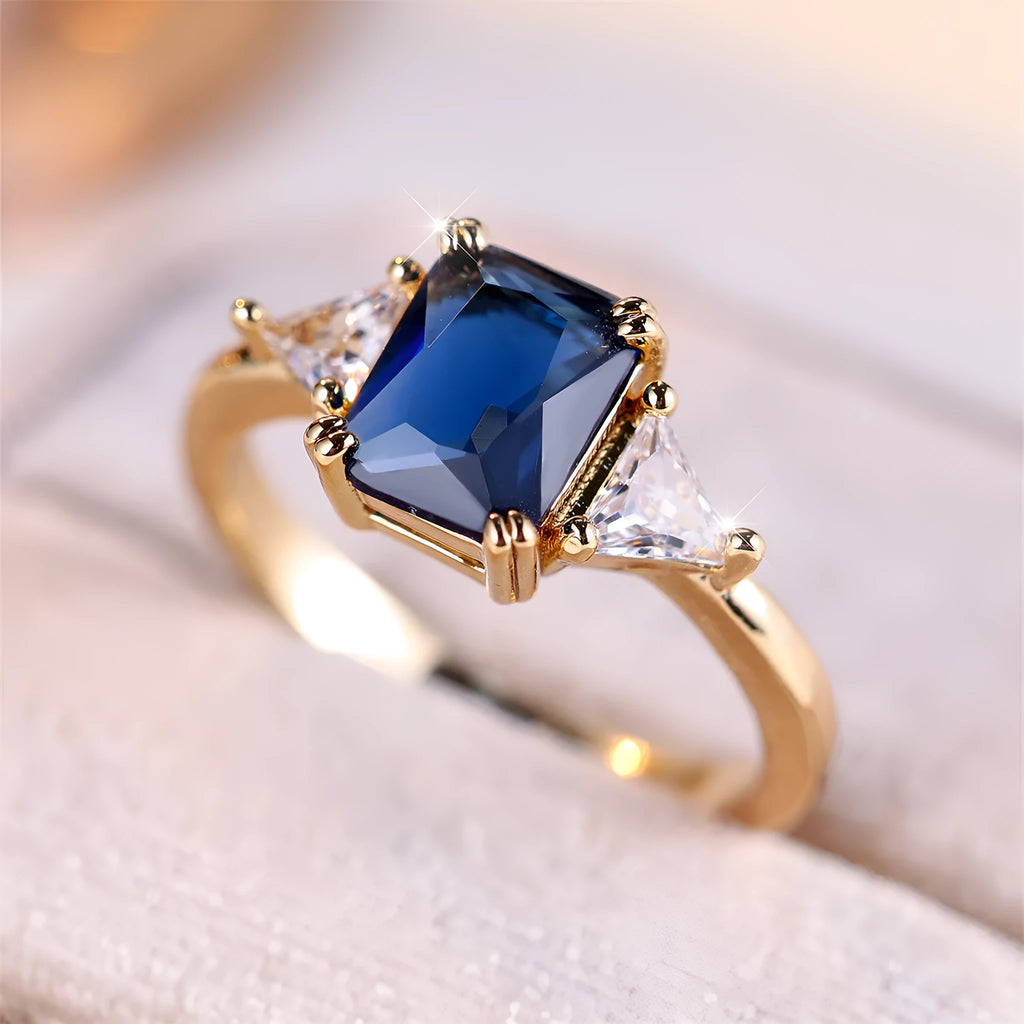 Women's rectangular copper ring in gold sapphire blue on a neutral background, showing its geometric band shape.