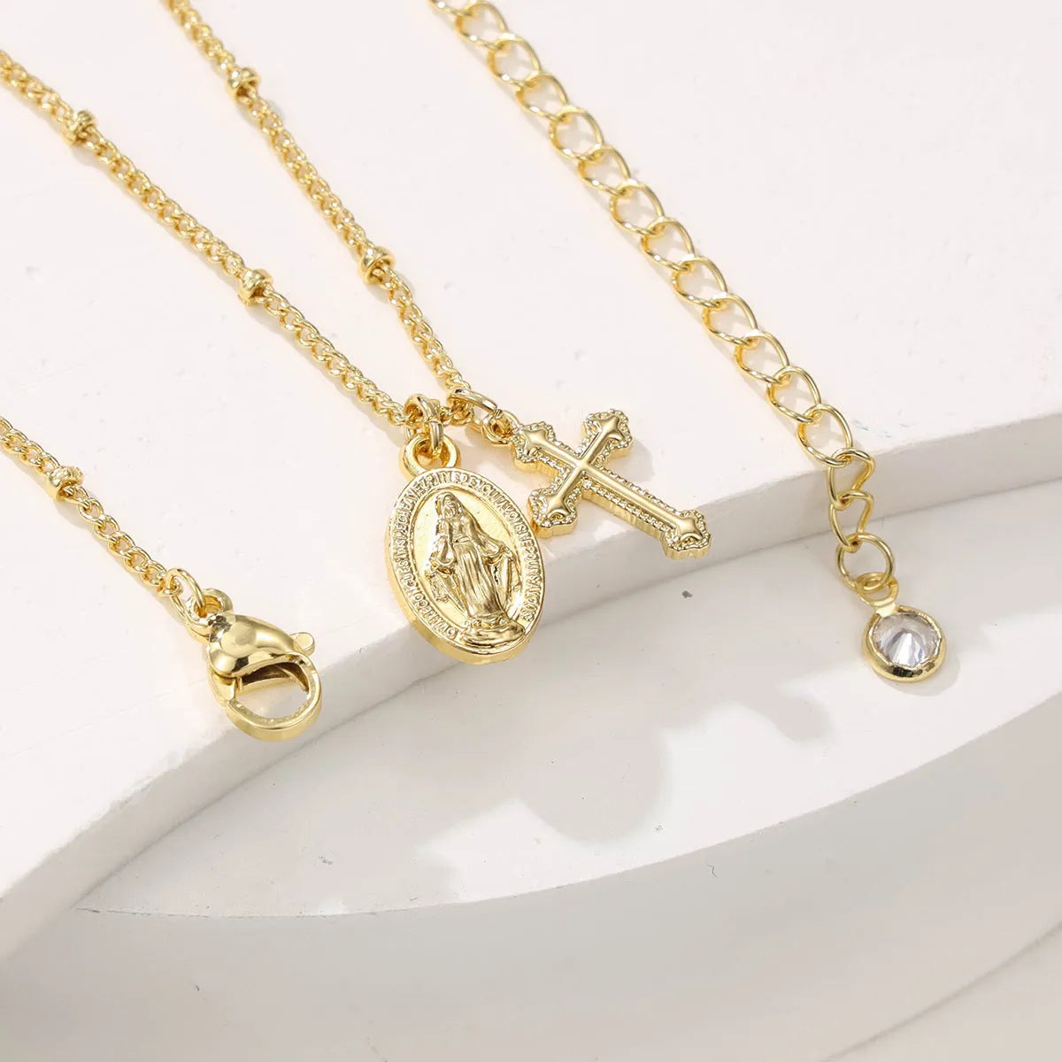 Gold geometric cross necklace with a Virgin Mary ornament pendant on a chain.