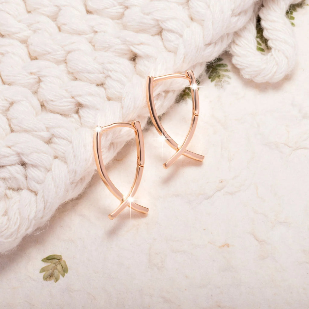A pair of rose gold coloured cross shaped copper earrings on a plain background.