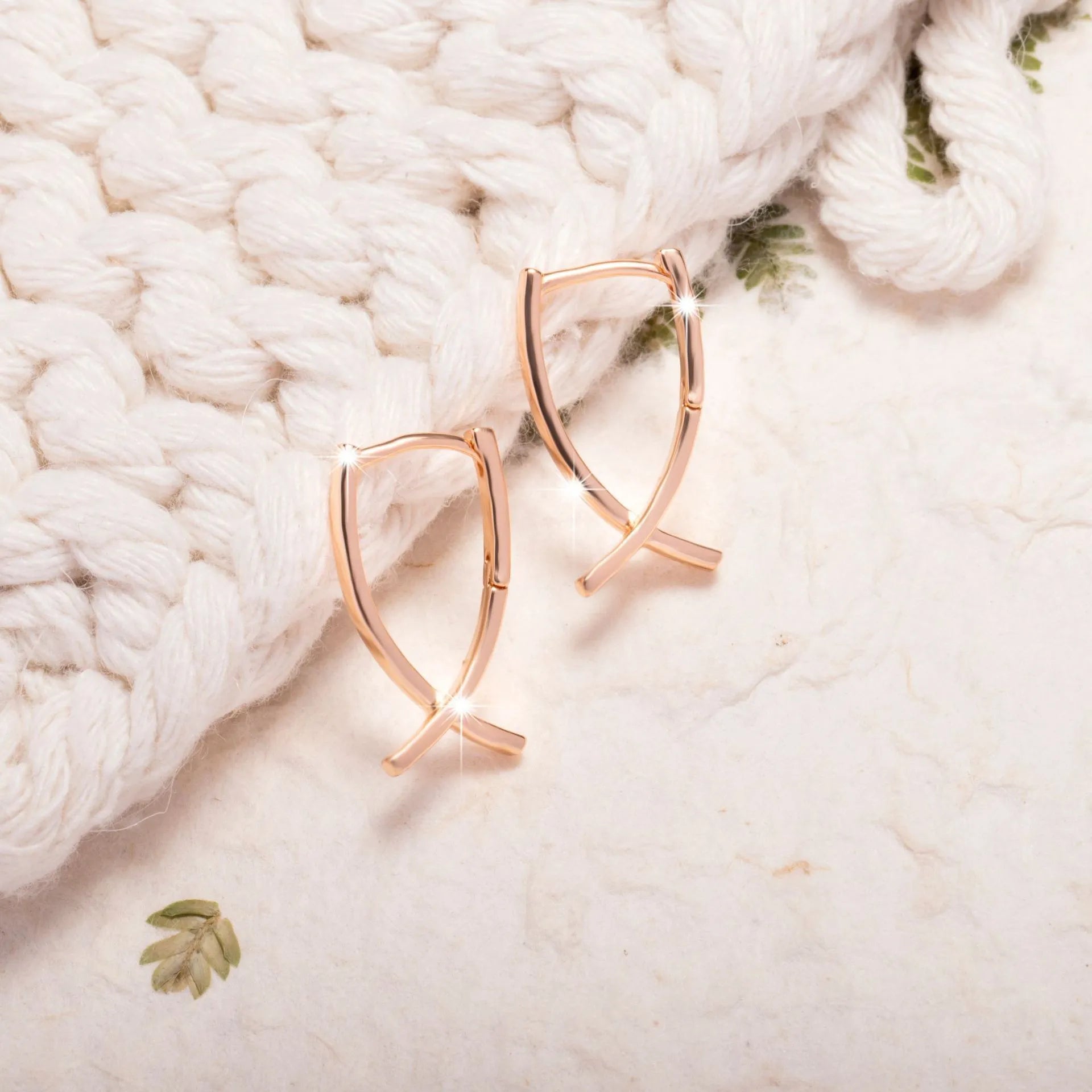 A pair of rose gold coloured cross shaped copper earrings on a plain background.