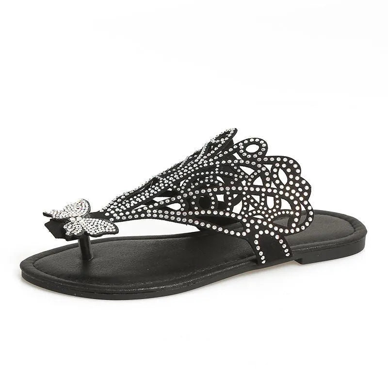 Women's black slip-on sandals with rhinestone decoration and hollow-out design on a flat rubber sole.