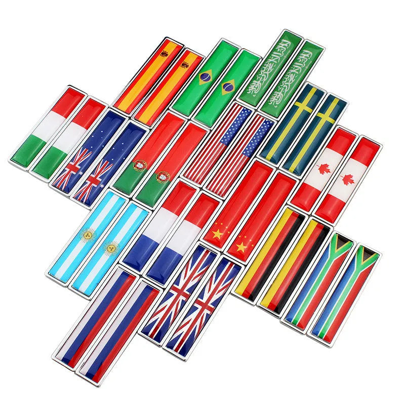 A pair of silver zinc alloy car badge labels with coloured national flag designs, shown at 58mm by 14mm scale.