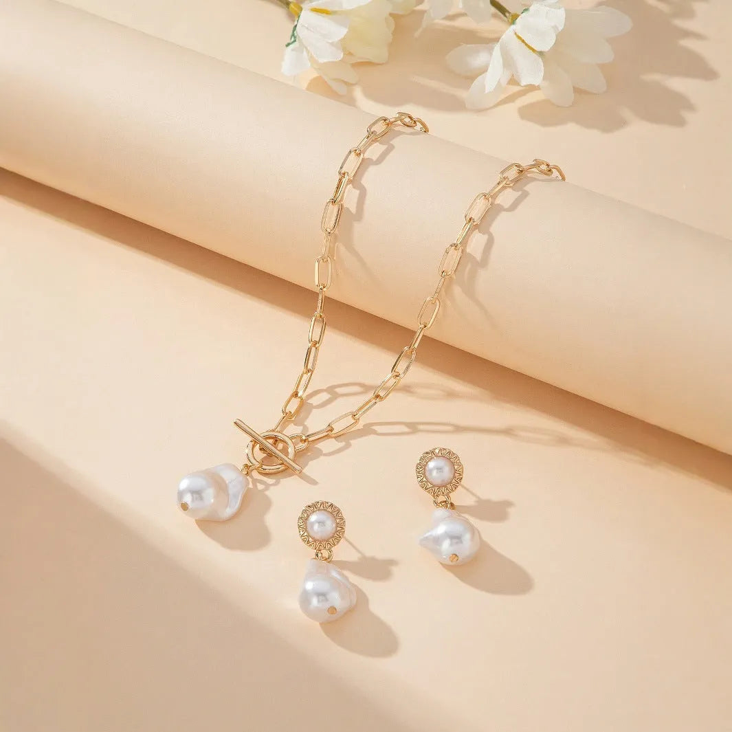 Gold-colour retro baroque pearl pendant necklace and matching ear studs set on a flat surface.