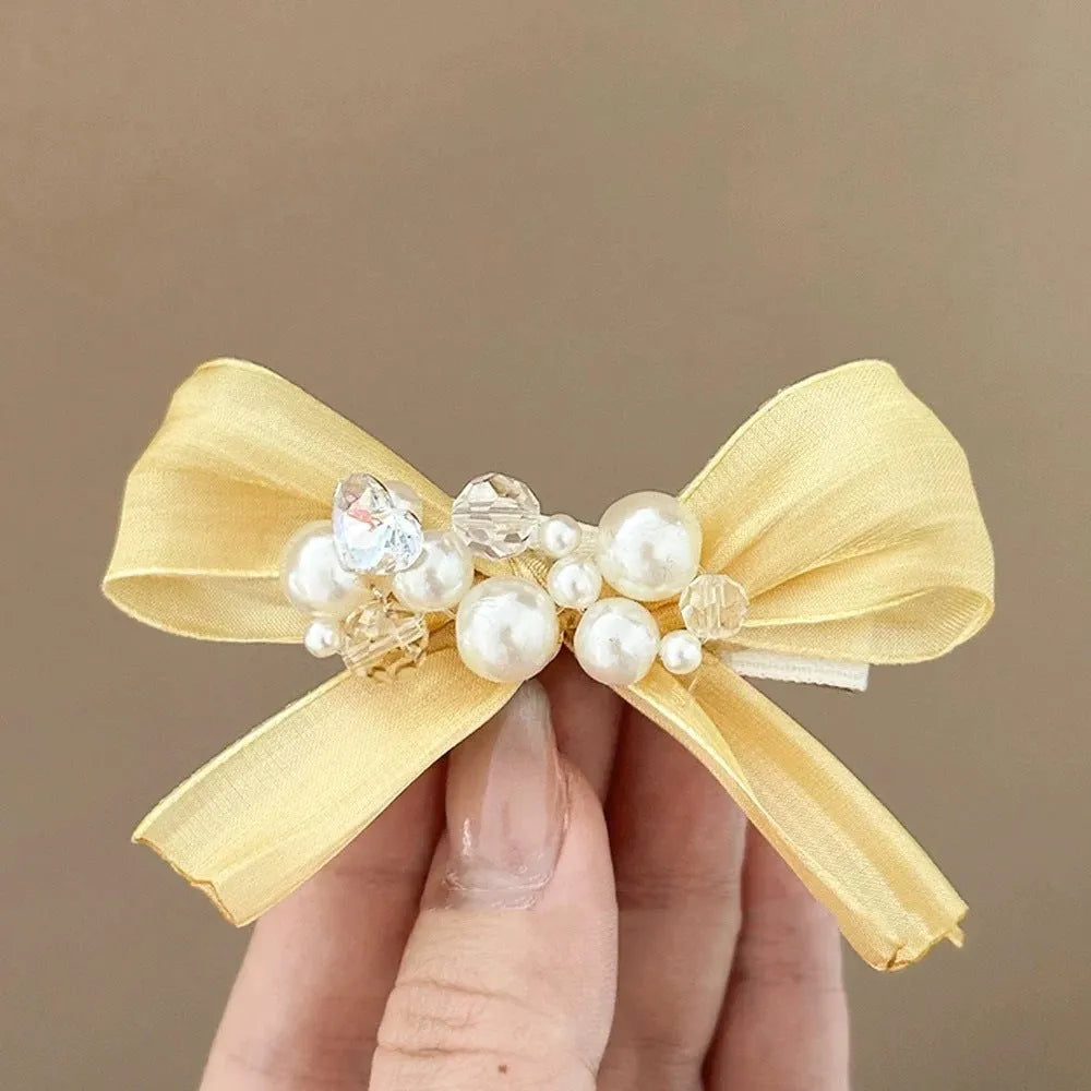 Yellow cloth bow hair clip with pearl accents on a duckbill clip.