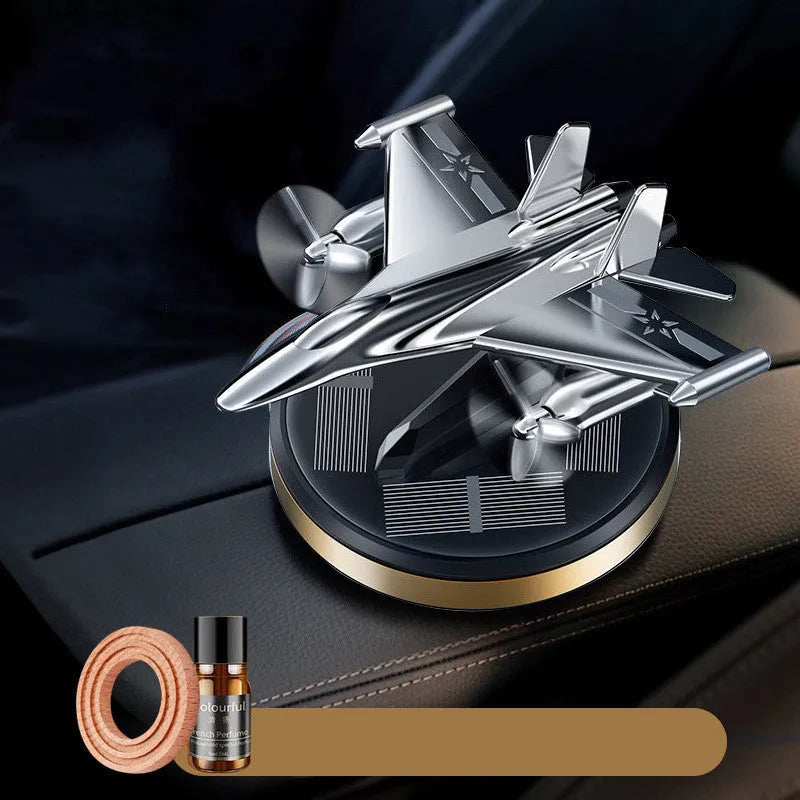 Silver solar-powered rotating fighter jet perfume ornament on a wooden surface.