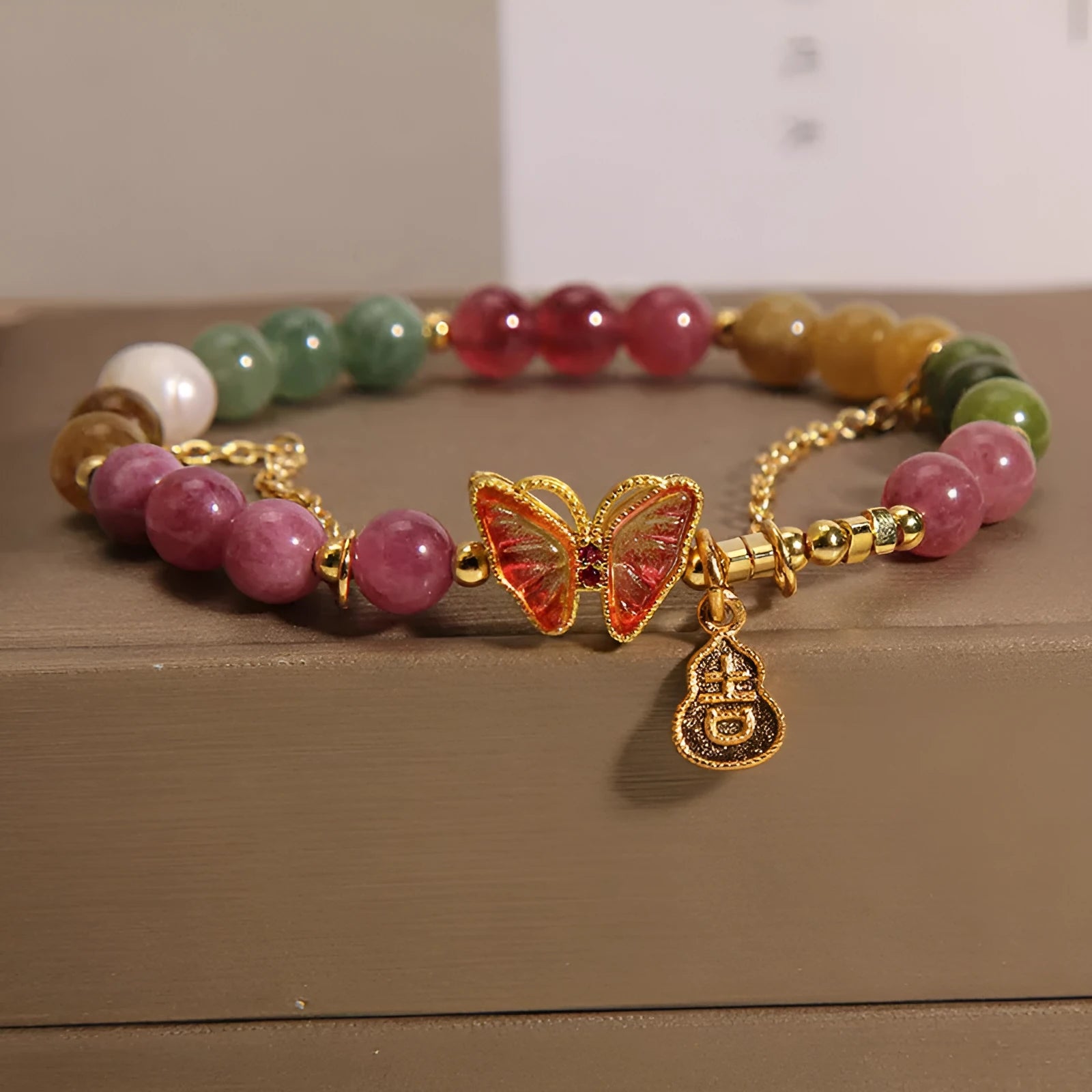 Close-up of a women's agate bracelet with a green tourmaline butterfly-shaped gourd charm on a white background.