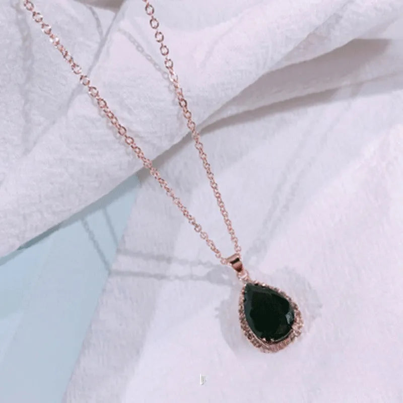 Close-up of a rose gold tone drop shape necklace with rhinestone details on a geometric pendant.