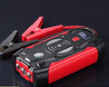 Red car emergency jump starter power pack with battery clamps and cables on a black storage box.