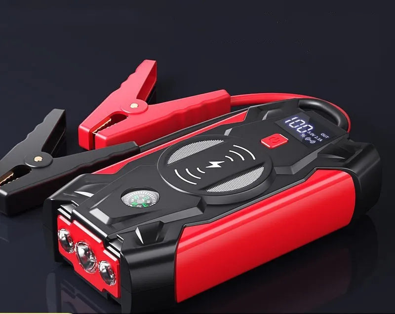 Red car emergency jump starter power pack with battery clamps and cables on a black storage box.