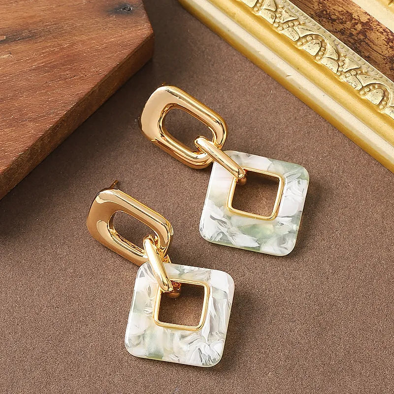 A pair of hollow square geometric earrings with a chamfered edge pattern in a gold tone finish.