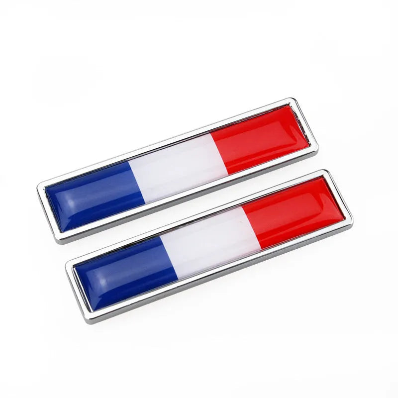 A pair of silver zinc alloy car badge labels with coloured national flag designs, shown at 58mm by 14mm scale.
