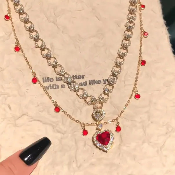 Gold tone double chain necklace with a central red love pearl pendant on an adjustable chain.