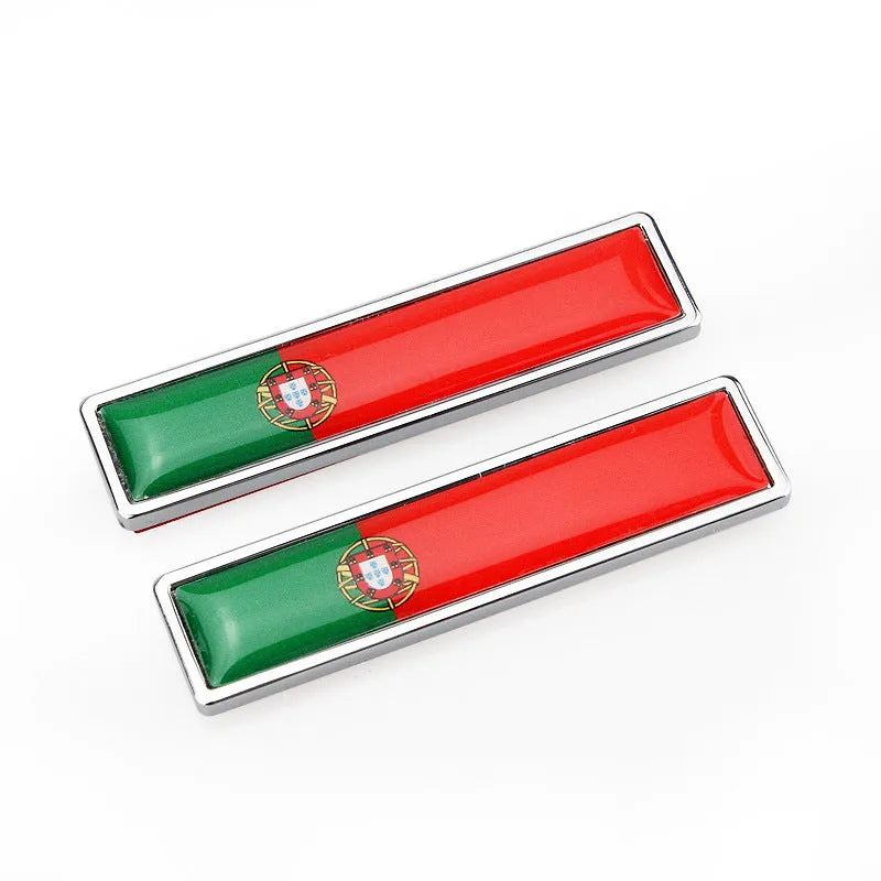 A pair of silver zinc alloy car badge labels with coloured national flag designs, shown at 58mm by 14mm scale.