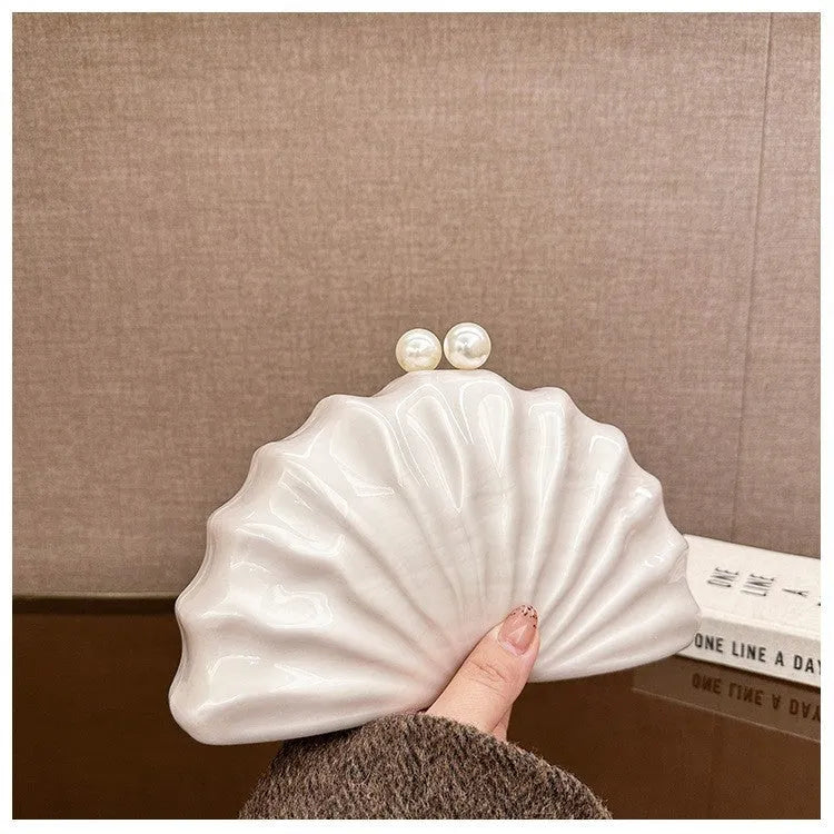 Acrylic shell-shaped clutch bag in champagne colour with chain detail on solid background