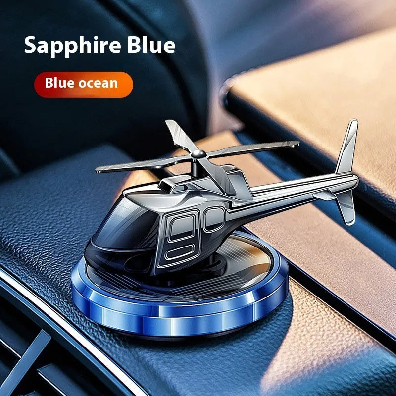 Silver metal solar-powered helicopter car air freshener rotating on a car dashboard.