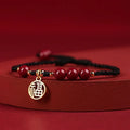 Cinnabar braided rope bracelet with blessing card, shown in black, red, or wine red with round bead or flower charm.