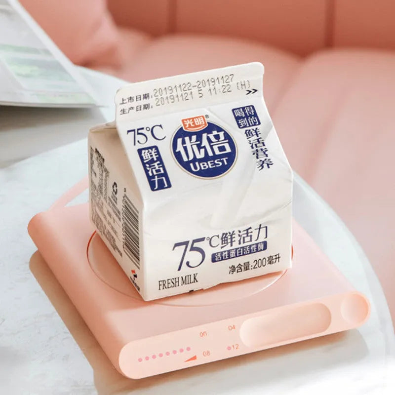 Pink and white USB heating cup pad or mug warmer with mechanical controls on a desk.