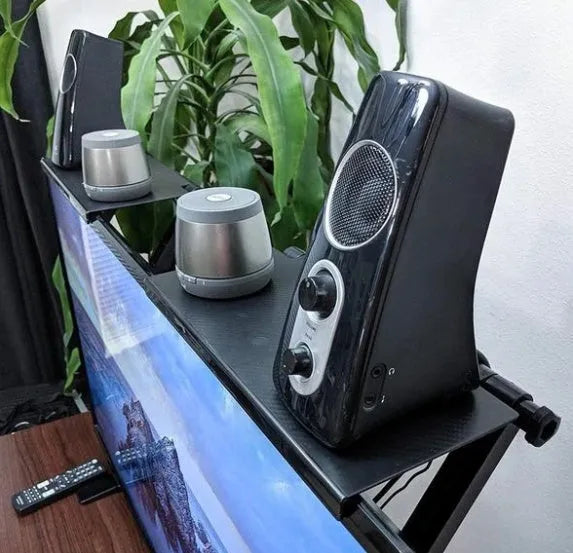 Black adjustable screen top shelf mounted on a monitor holding a streaming device and remote