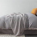 Small light grey polyester throw blanket folded on a sofa, showing its compact 127x170cm size.