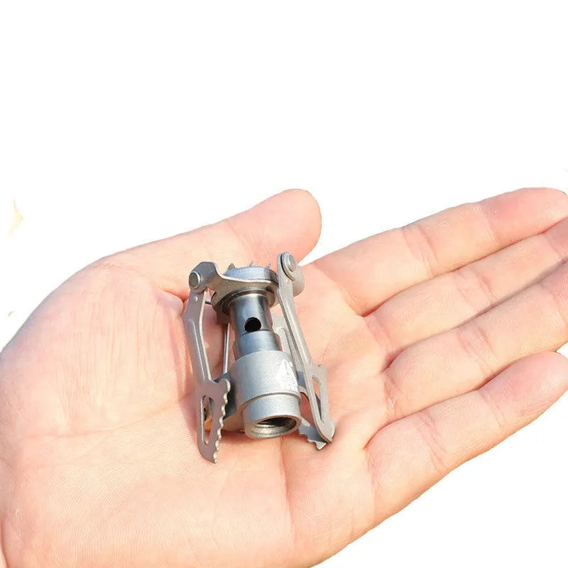 Silver portable propane camping stove with one-piece burner unit on a flat surface.