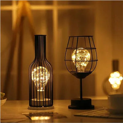 Minimalist hollow wrought iron table lamp in red wine bottle shape with warm white light on a desk