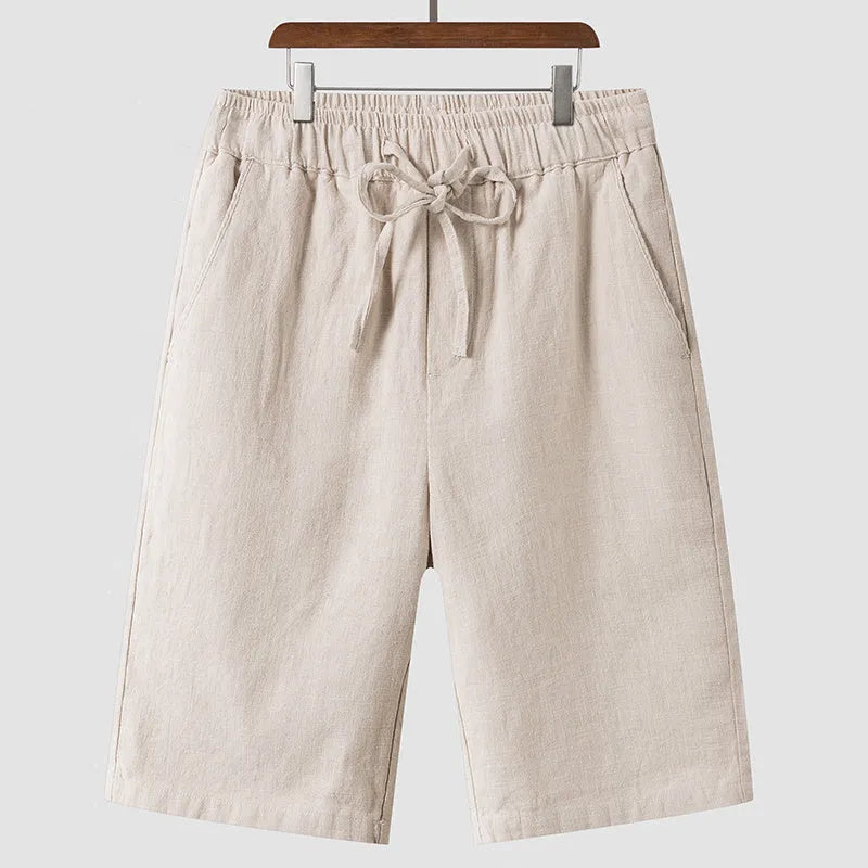 Men's beige linen shorts with loose cropped leg and elasticated waistband on a neutral background.