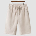 Men's beige linen shorts with loose cropped leg and elasticated waistband on a neutral background.