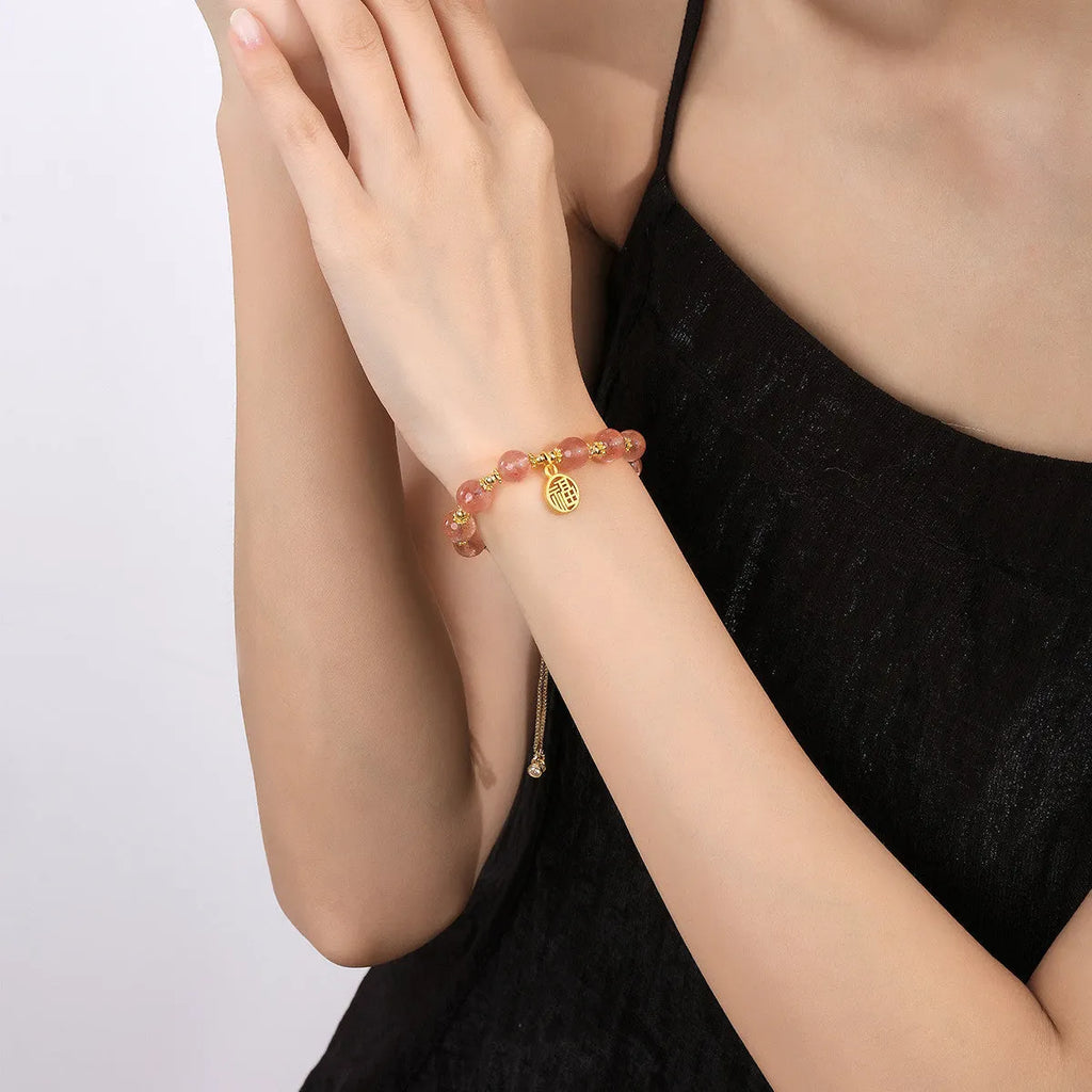 A geometric crystal bracelet in strawberry quartz colour with a fu character detail.
