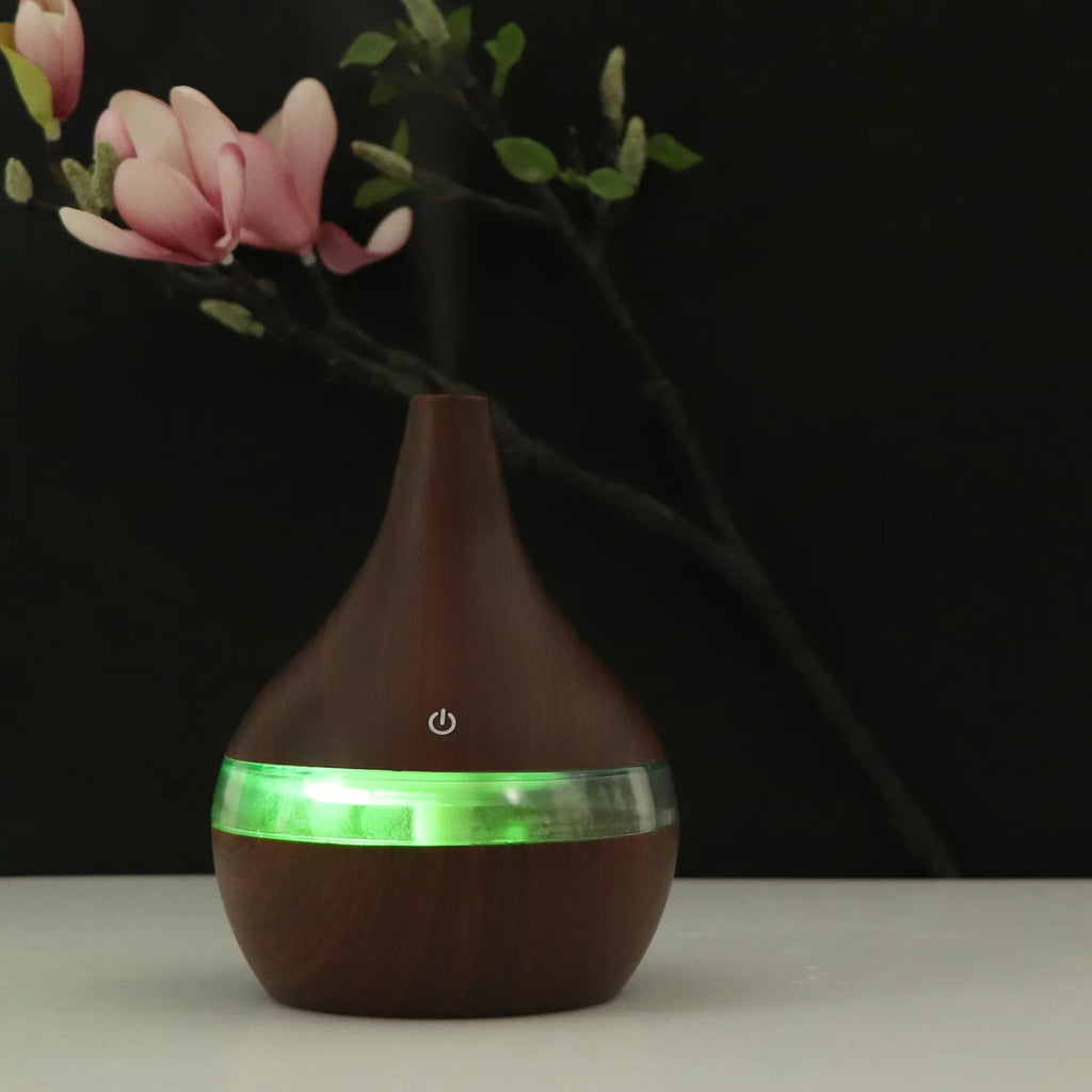 A columnar USB air humidifier with a wood grain finish, remote control, and USB cable on a desktop.
