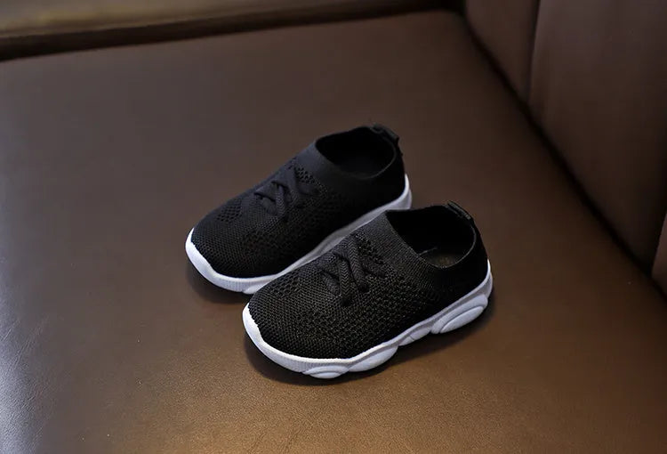 Children's fabric lazy shoe with a non-slip rubber sole, shown in colour options of white, black, pink, and grey.