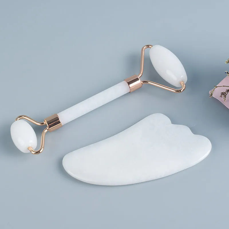 White jade facial roller and gua sha scraper tools placed on a smooth wooden storage board.