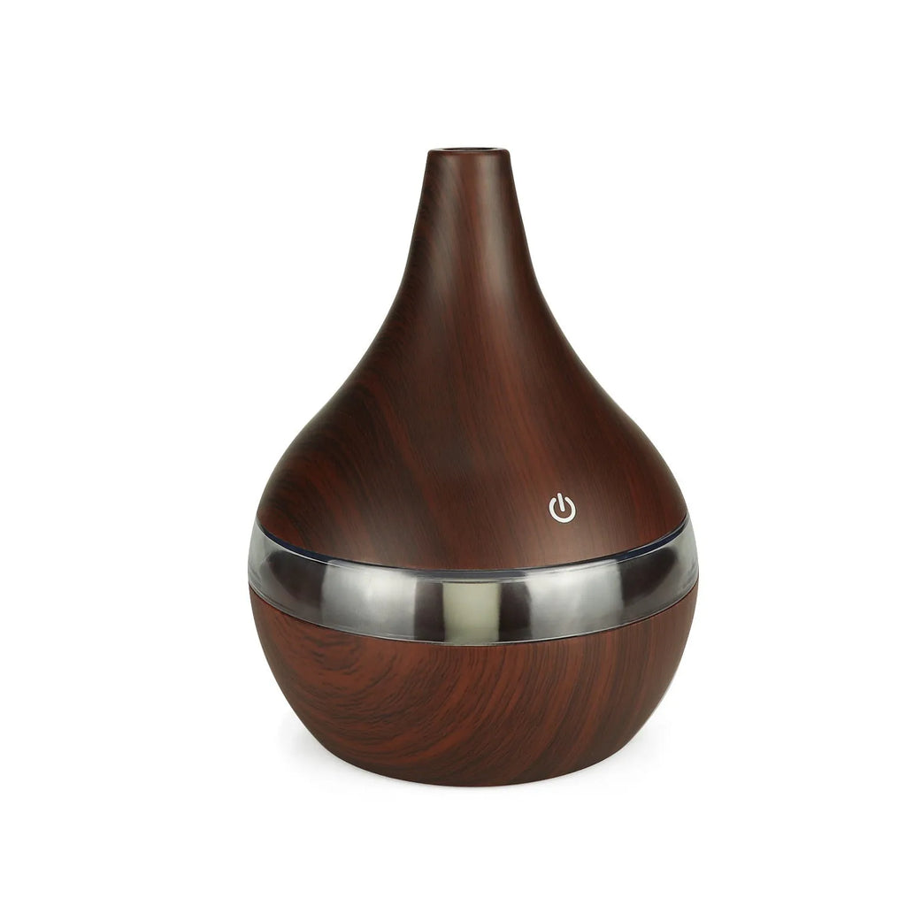 A columnar USB air humidifier with a wood grain finish, remote control, and USB cable on a desktop.