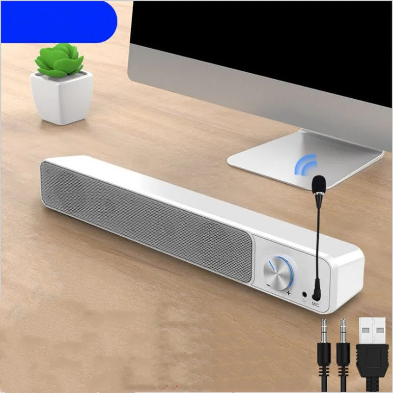 Compact black and white desktop computer speaker with audio and USB cables on a wooden desk.