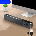 Compact black and white desktop computer speaker with audio and USB cables on a wooden desk.