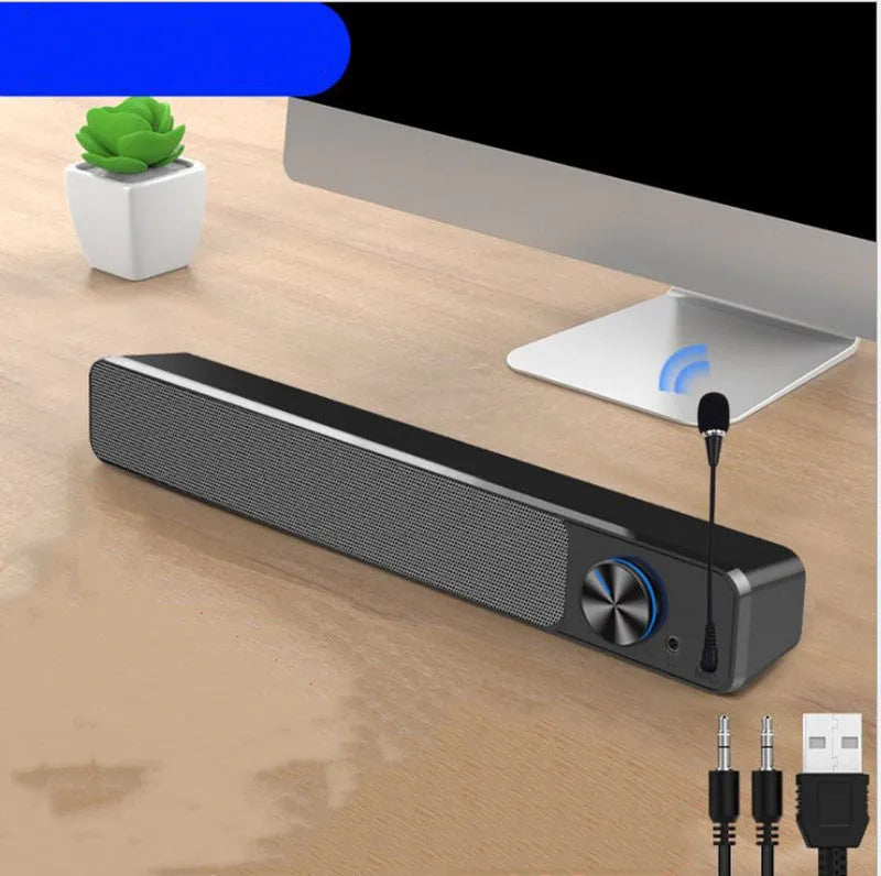 Compact black and white desktop computer speaker with audio and USB cables on a wooden desk.