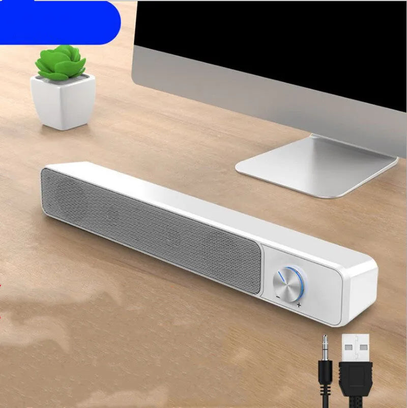 Compact black and white desktop computer speaker with audio and USB cables on a wooden desk.