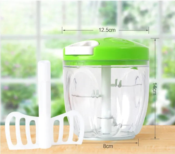 Green manual kitchen chopper with stainless steel blades next to chopped vegetables on a counter.
