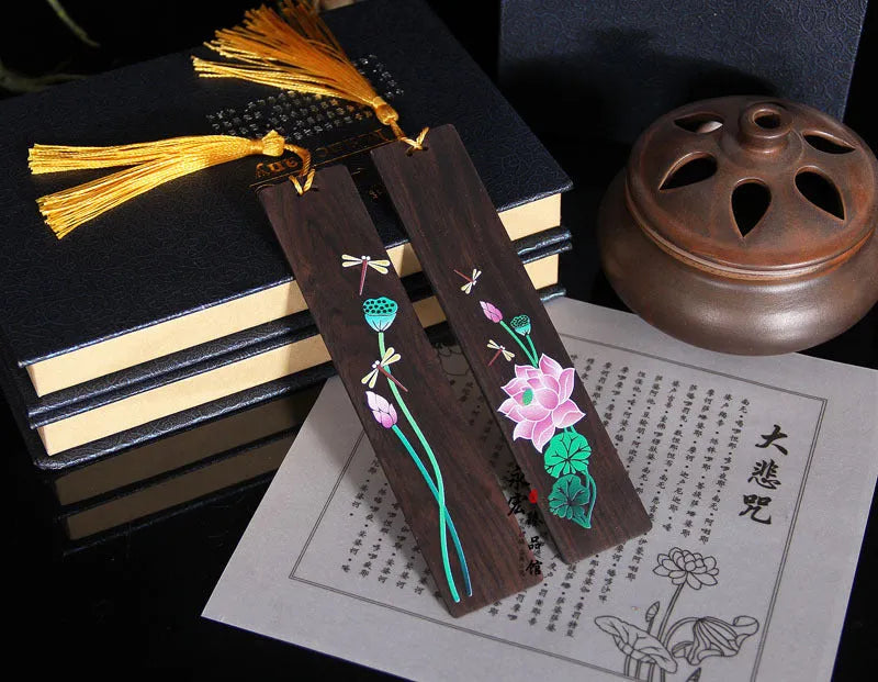 Close-up of a hand-painted lotus design on a polished sandalwood Chinese bookmark with hanging cord.