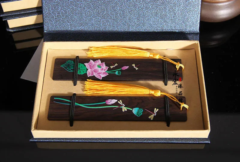 Close-up of a hand-painted lotus design on a polished sandalwood Chinese bookmark with hanging cord.