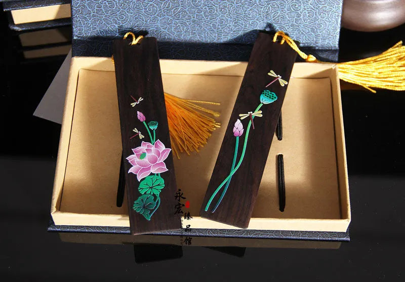 Close-up of a hand-painted lotus design on a polished sandalwood Chinese bookmark with hanging cord.