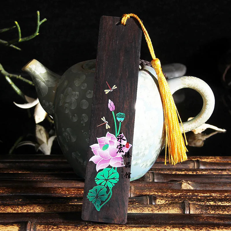 Close-up of a hand-painted lotus design on a polished sandalwood Chinese bookmark with hanging cord.