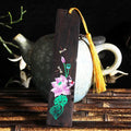 Close-up of a hand-painted lotus design on a polished sandalwood Chinese bookmark with hanging cord.