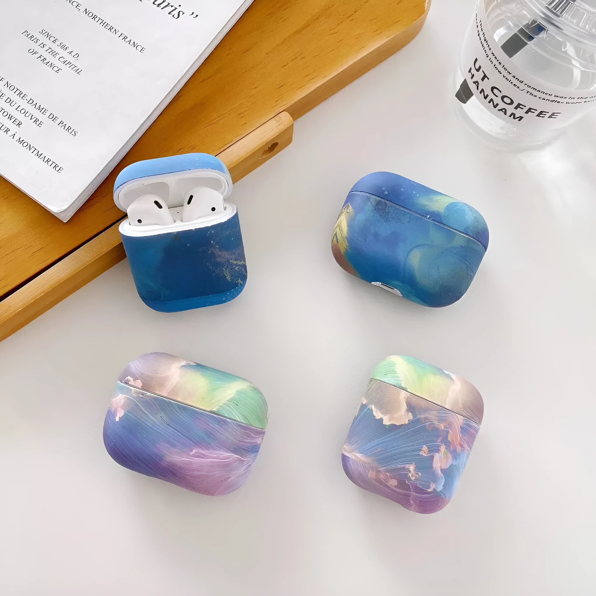 Hard plastic protective sleeve for AirPods case in a pink watercolour design, shown next to a blue watercolour version.