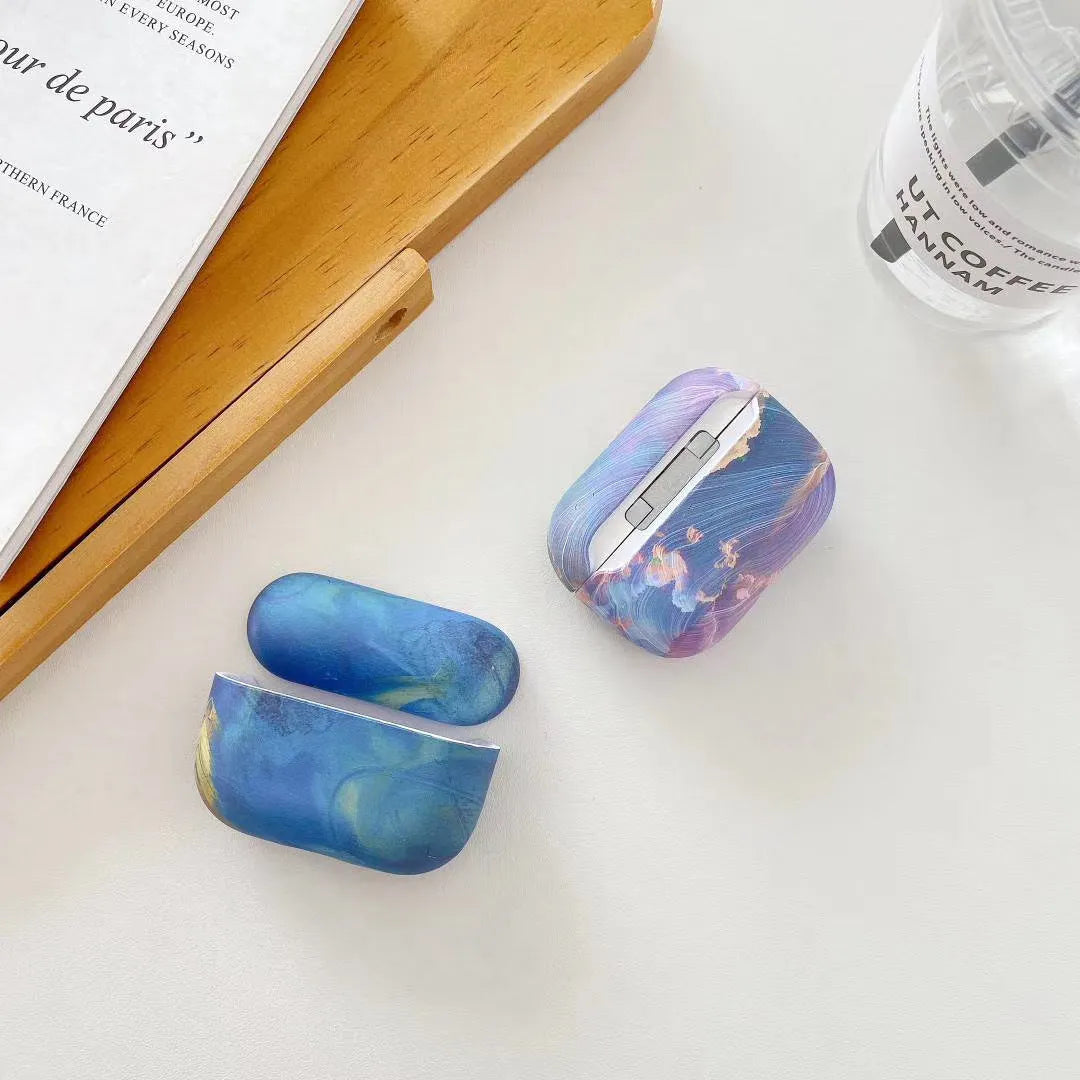 Hard plastic protective sleeve for AirPods case in a pink watercolour design, shown next to a blue watercolour version.