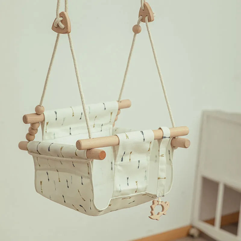 Natural beige cotton canvas baby swing chair with wooden seat and tassel pattern, hanging indoors.