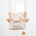 Natural beige cotton canvas baby swing chair with wooden seat and tassel pattern, hanging indoors.