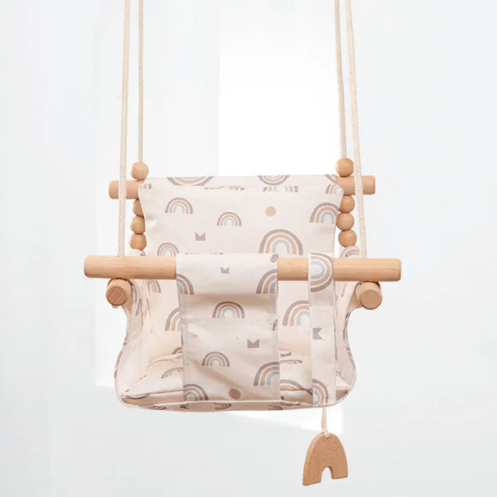 Natural beige cotton canvas baby swing chair with wooden seat and tassel pattern, hanging indoors.