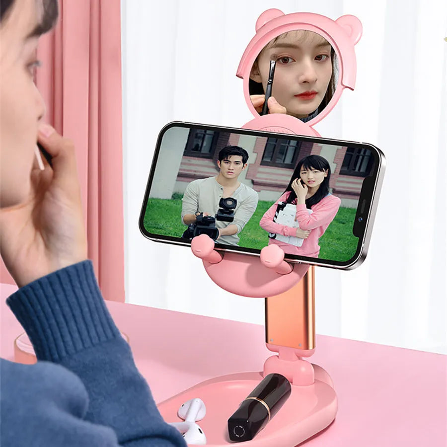 Blue adjustable desk phone holder with mirror, holding an iPhone at an angle on a wooden desk